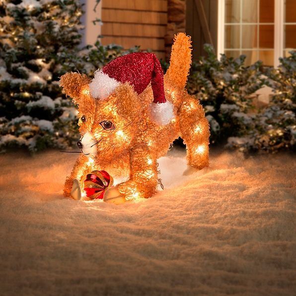 cat christmas yard decor A fluffy, Santa hat wearing, feline happily plays with a Christmas